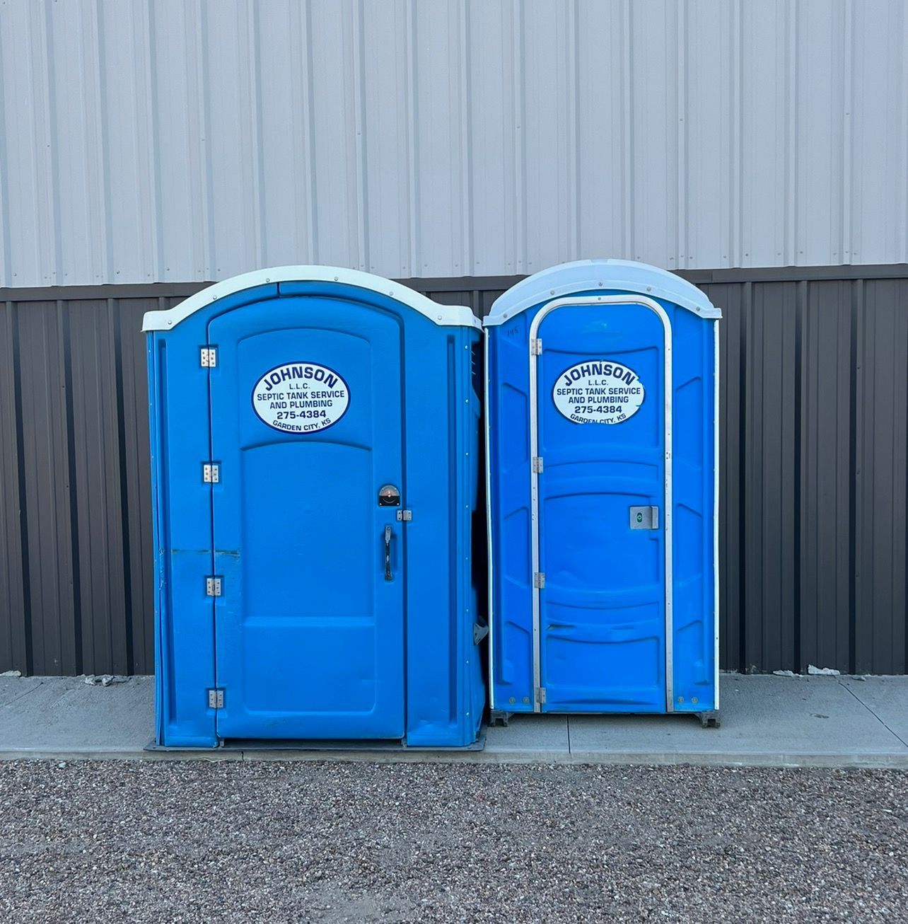 Two blue portable toilets in front of a gray and white building.