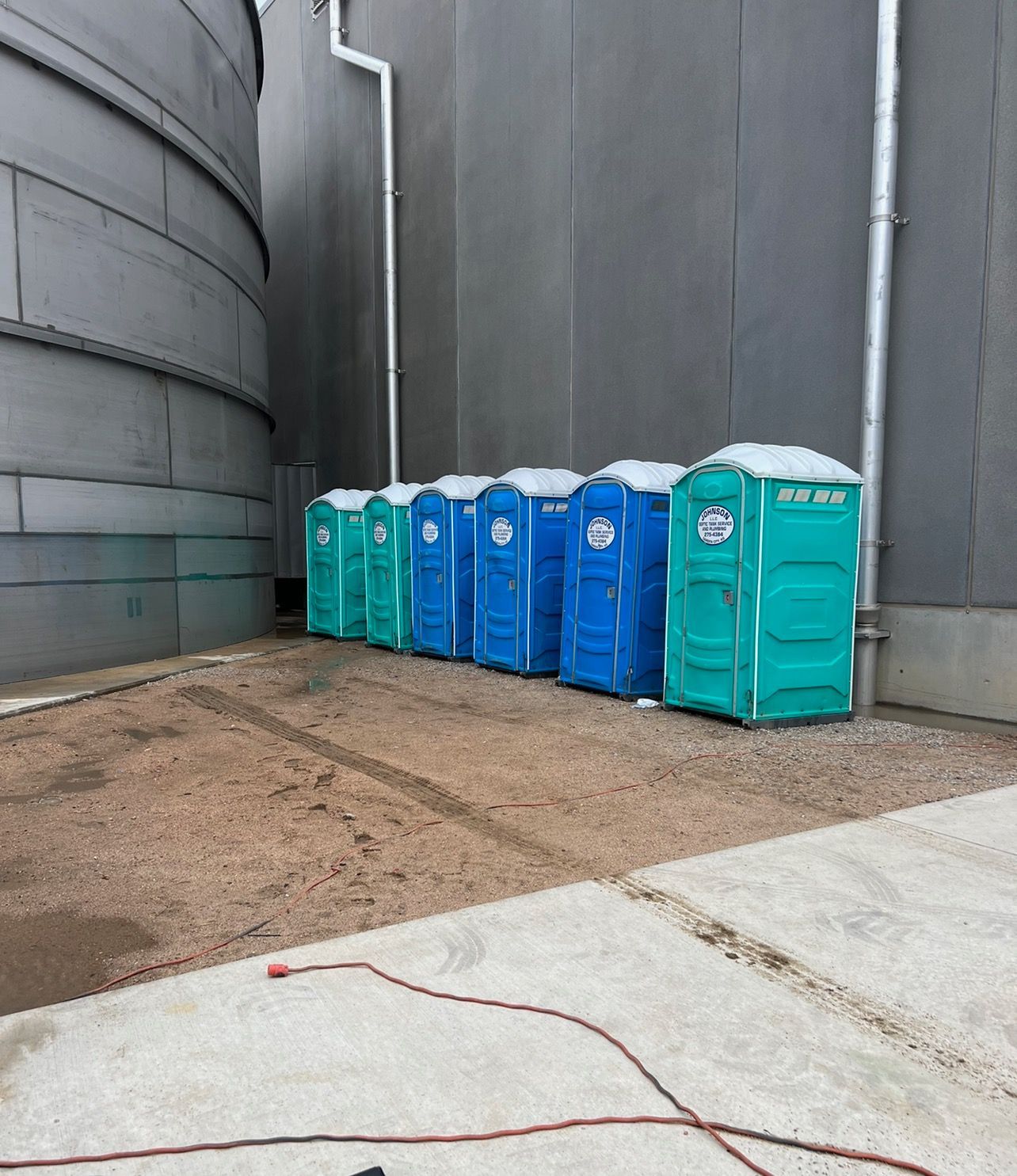 Row of blue and green portable toilets next to industrial building.