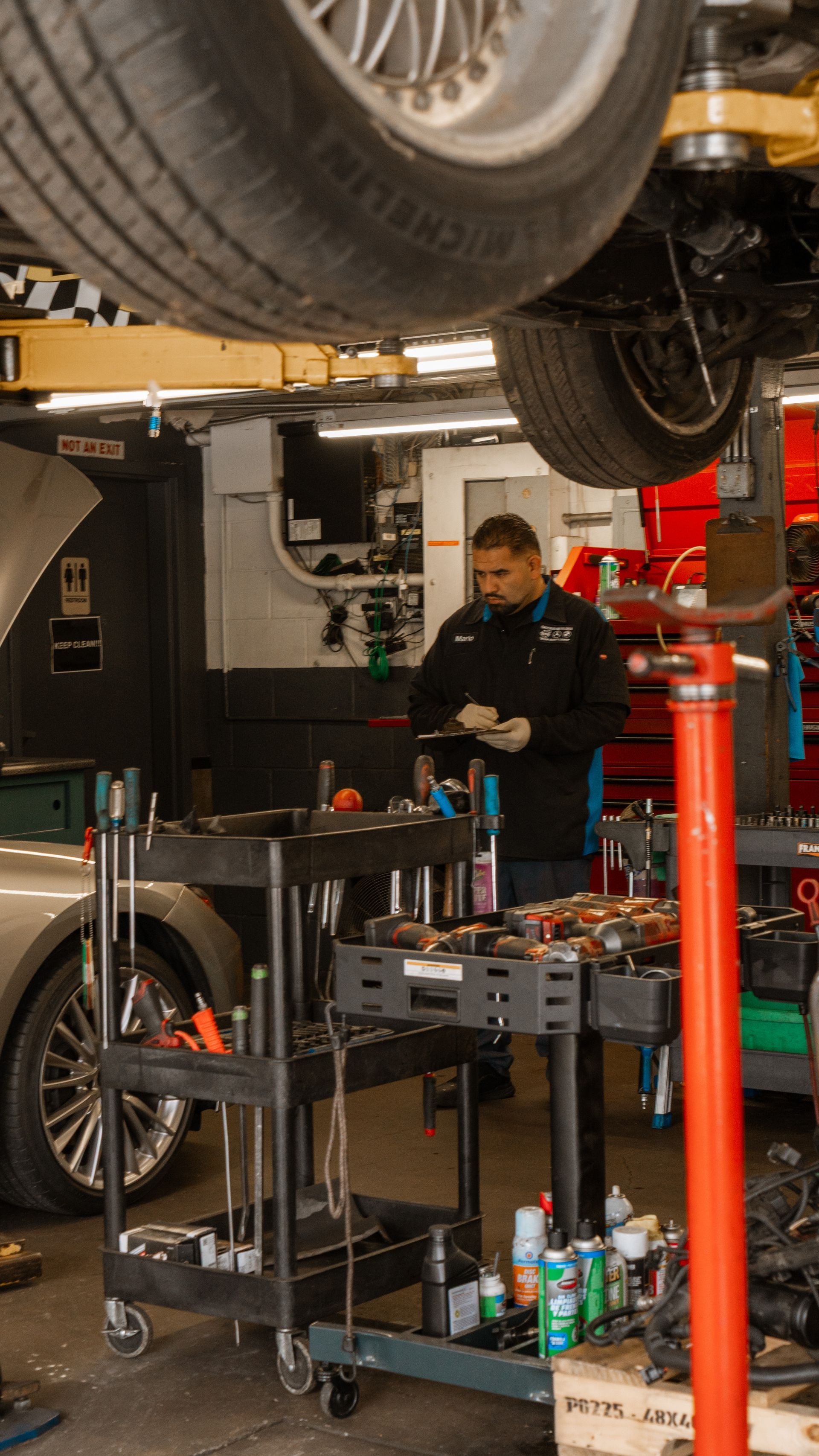 Mechanic working on a car in a garage with tools and equipment visible on a workbench.