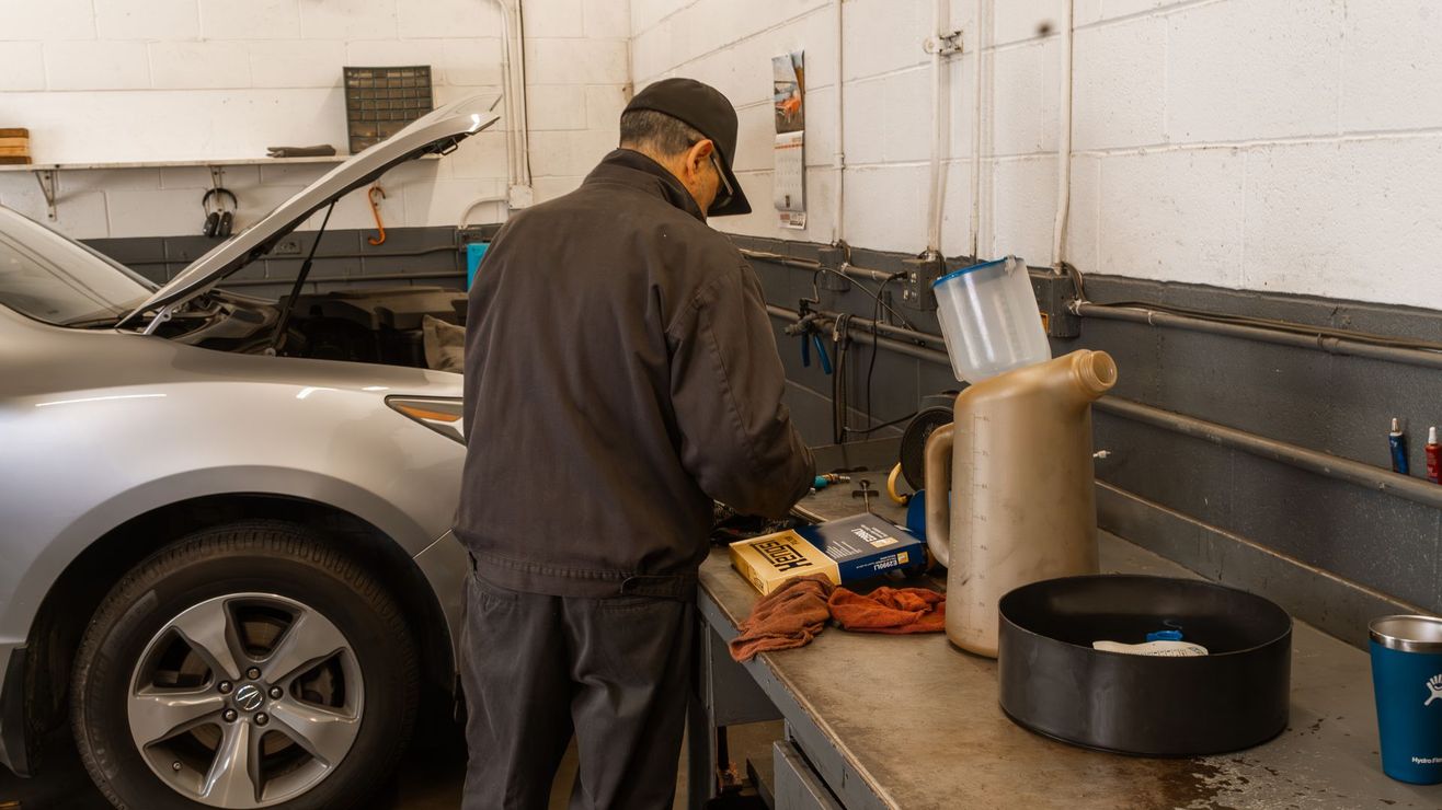 Mechanic working on a car in a garage. Car is silver, workbench has tools and containers.