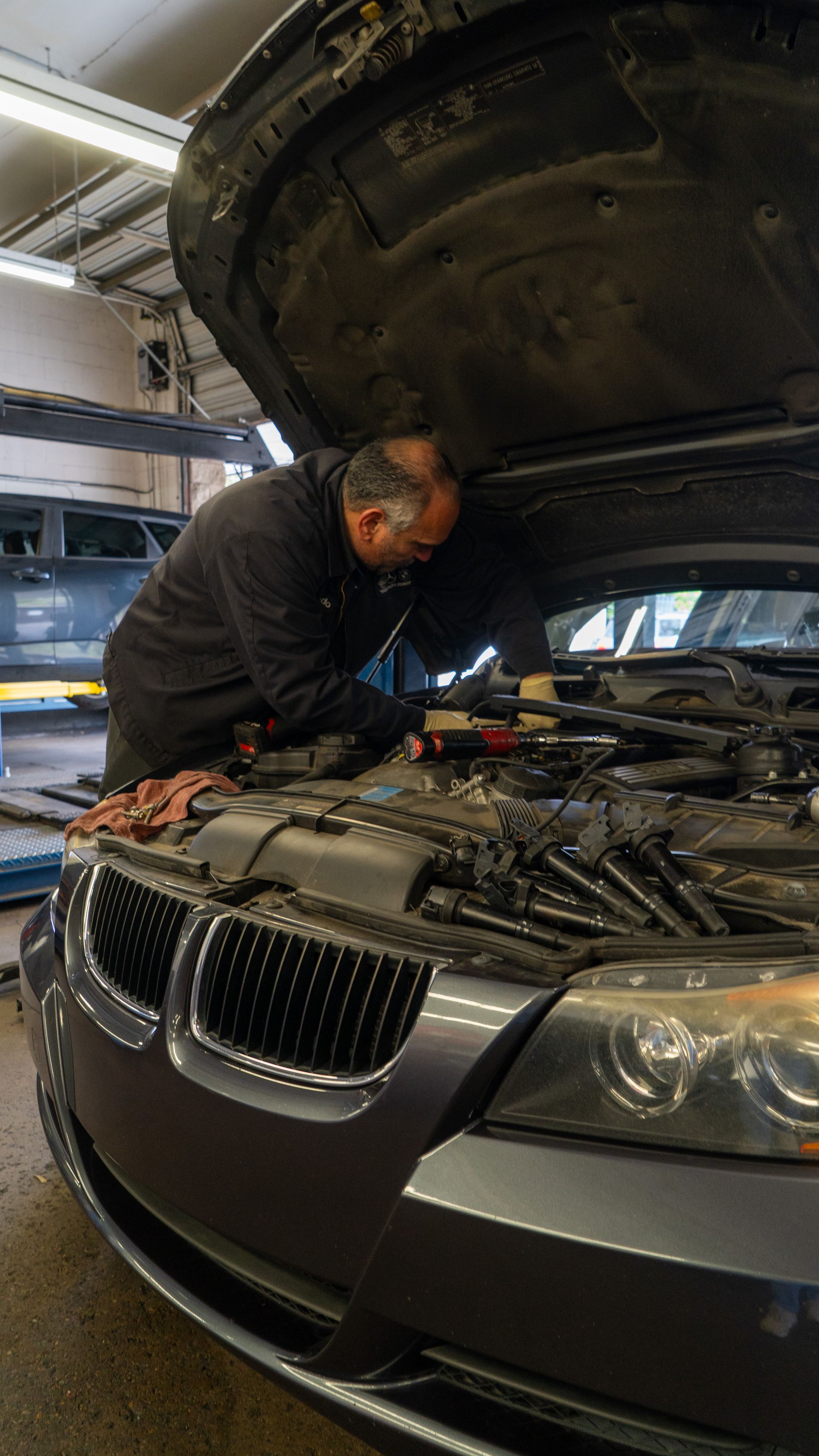 Mechanic inspecting a BMW engine under the open hood in a garage