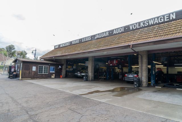 Auto repair shop with open bays, signage for BMW, Lexus, Jaguar, Audi, and Volkswagen.