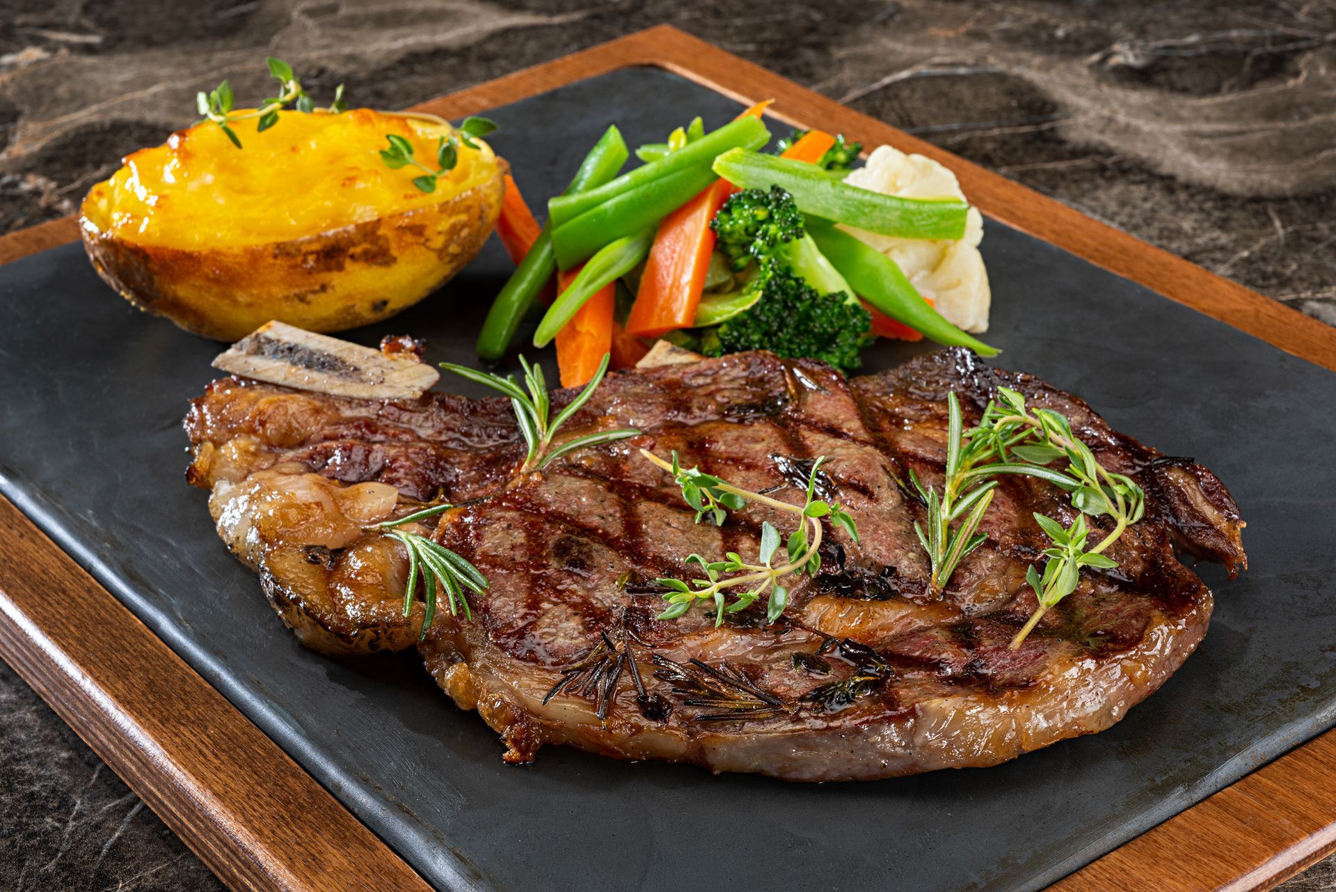 Una bistecca con verdure e una patata su un piatto nero.