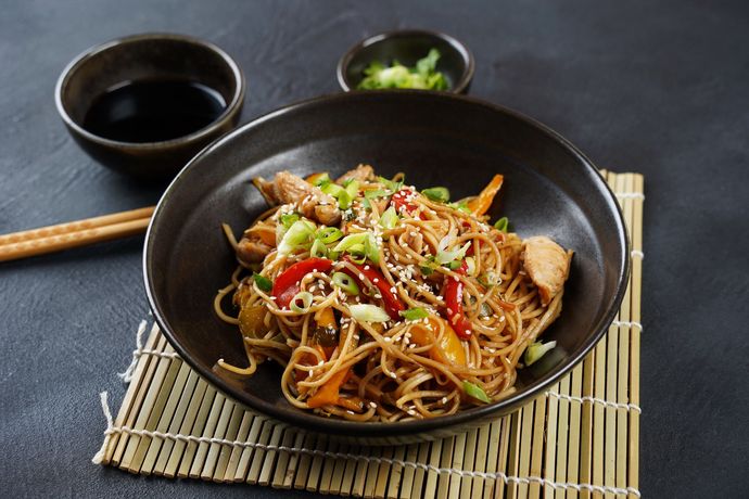 Una ciotola di noodles con carne e verdure su una stuoia di bambù con le bacchette.