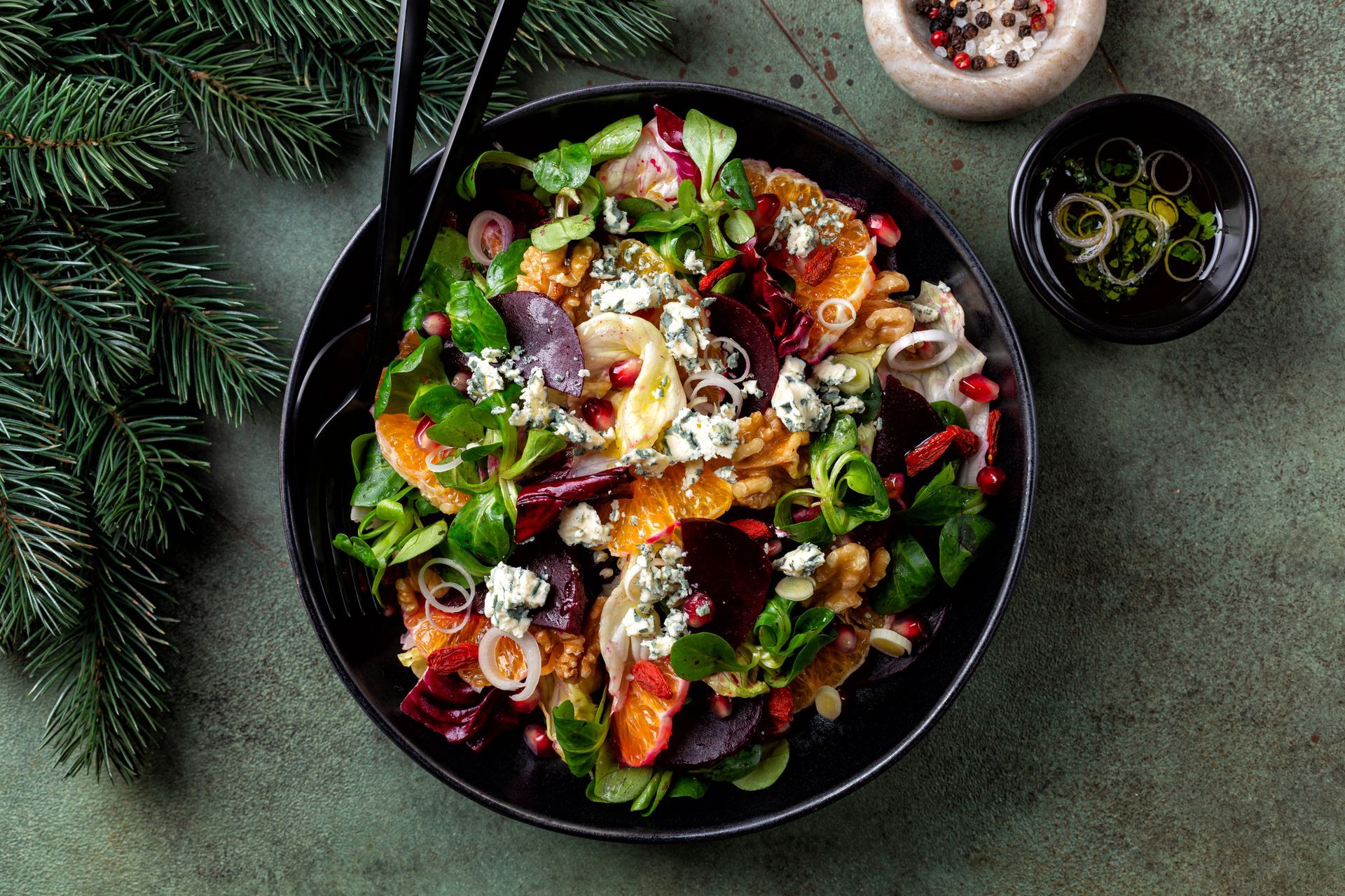 Un'insalata in una ciotola nera su un tavolo con un albero di Natale sullo sfondo.