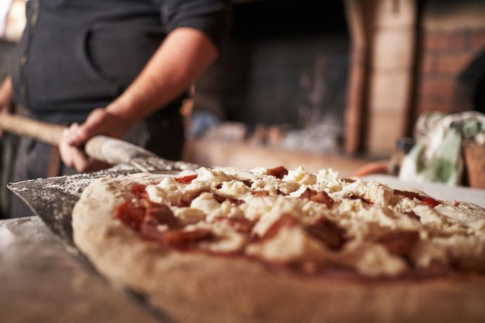 Una persona sta stendendo l'impasto della pizza con un mattarello di legno.