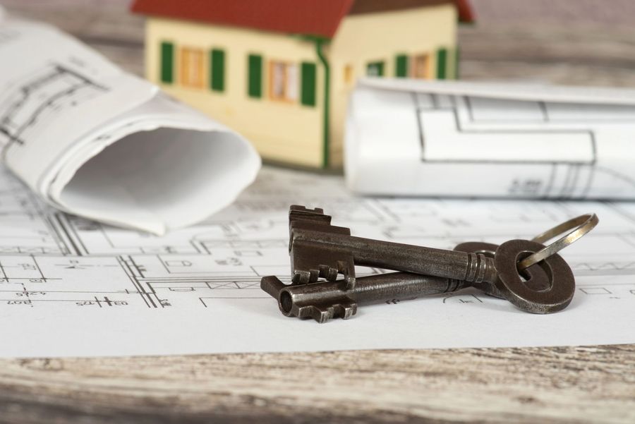 Le chiavi di casa su delle planimetrie accanto a un modellino di casa in miniatura, a suggerire un progetto di abitazione o un'operazione immobiliare.