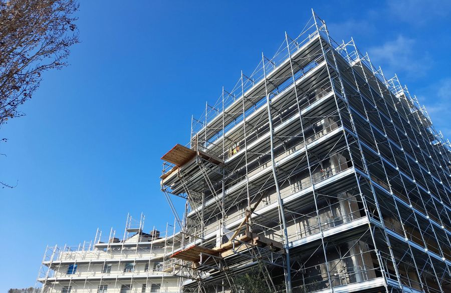 Impalcature attorno a un edificio a più piani in costruzione, sullo sfondo di un cielo azzurro e limpido.