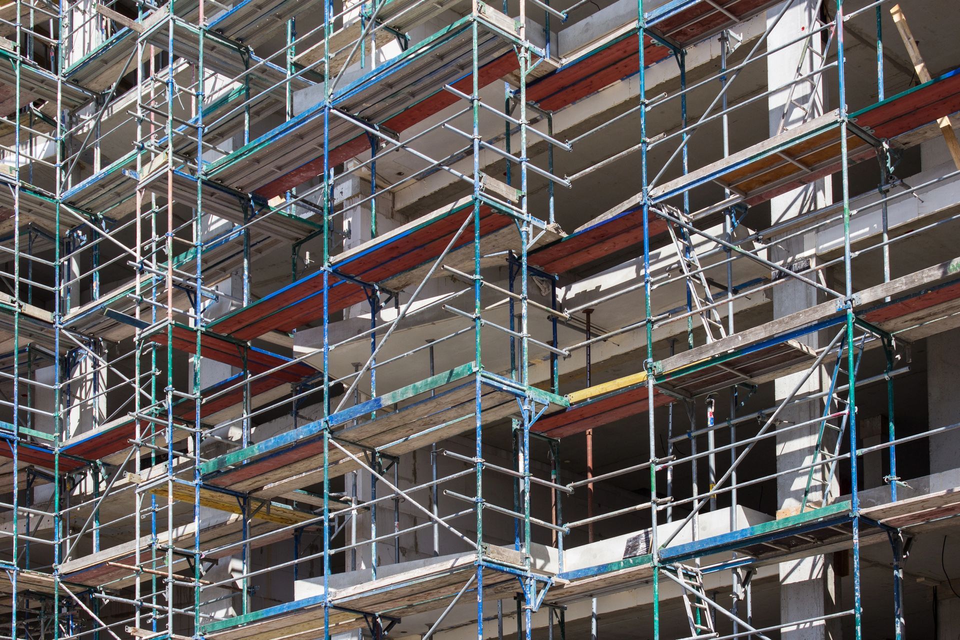 Ponteggi intorno a un edificio in costruzione, con reti di sicurezza blu e rosse e pavimenti in cemento a vista.