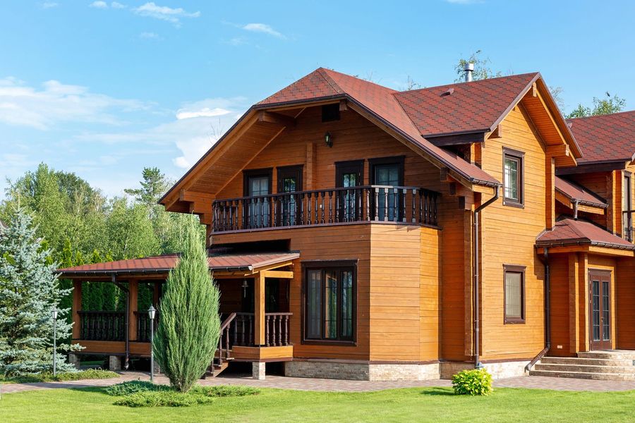 Casa moderna a due piani in legno con tetto rosso, balcone e prato verde sotto un cielo azzurro.