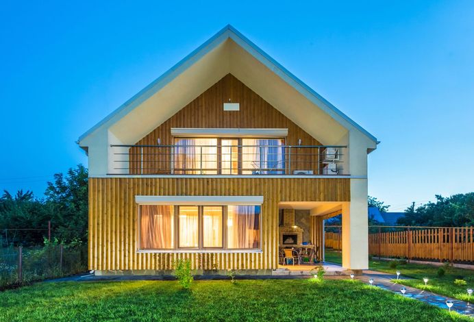 Casa moderna a due piani con luci calde, rivestimento in legno e balcone al crepuscolo