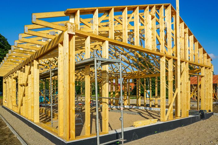Casa in costruzione con struttura in legno, travi del tetto a vista e cielo azzurro limpido.