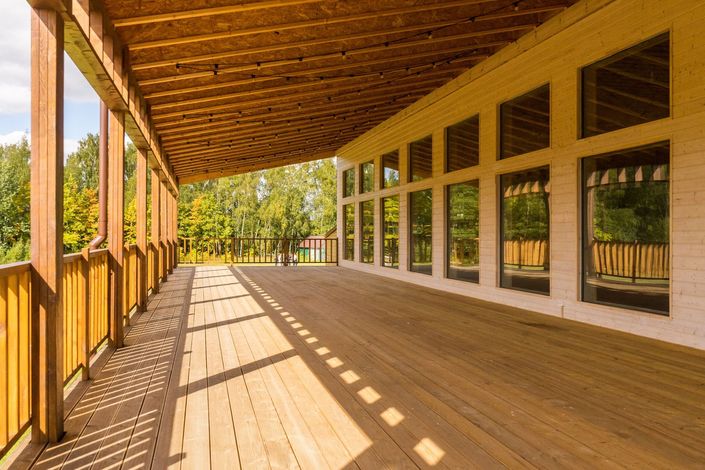 Veranda in legno con ringhiere e grandi finestre, illuminata da una calda luce solare che proietta lunghe ombre.