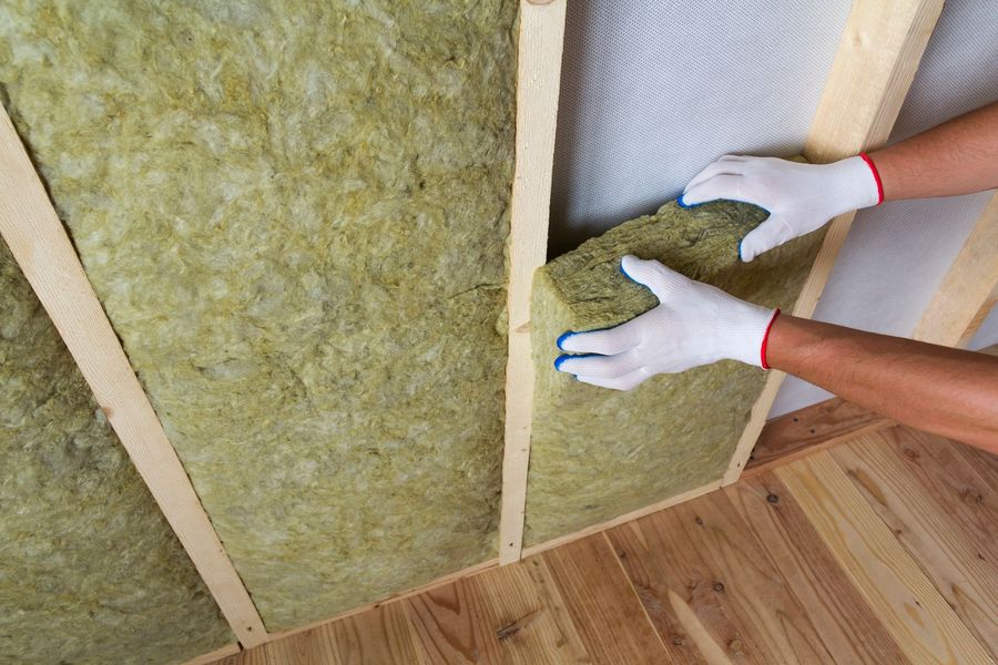 Mani che posizionano pannelli isolanti verdi tra i montanti in legno di una parete in costruzione in una stanza.