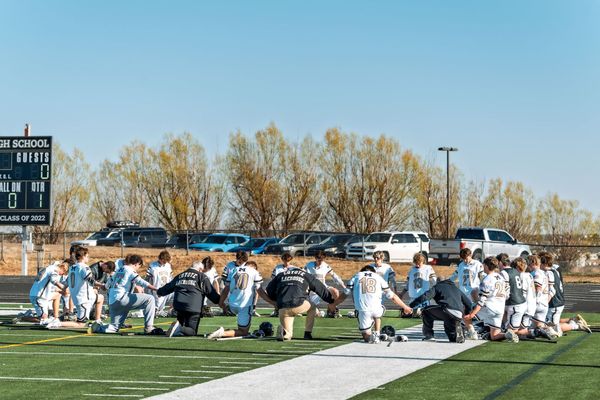 Football team kneeling on a field in white uniforms under a clear blue sky