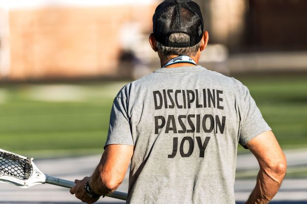 Tennis player seen from behind on a court, wearing a gray shirt reading “DISCIPLINE PASSION JOY”