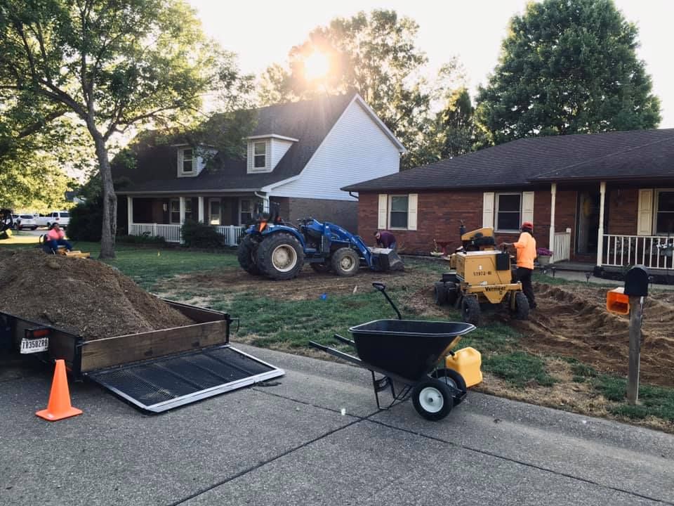 Construction crew with blue tractor and wheelbarrow working in a yard beside a house at sunset