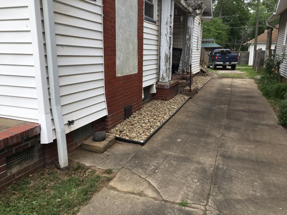 Narrow concrete driveway beside white brick houses, with a parked truck in the distance.