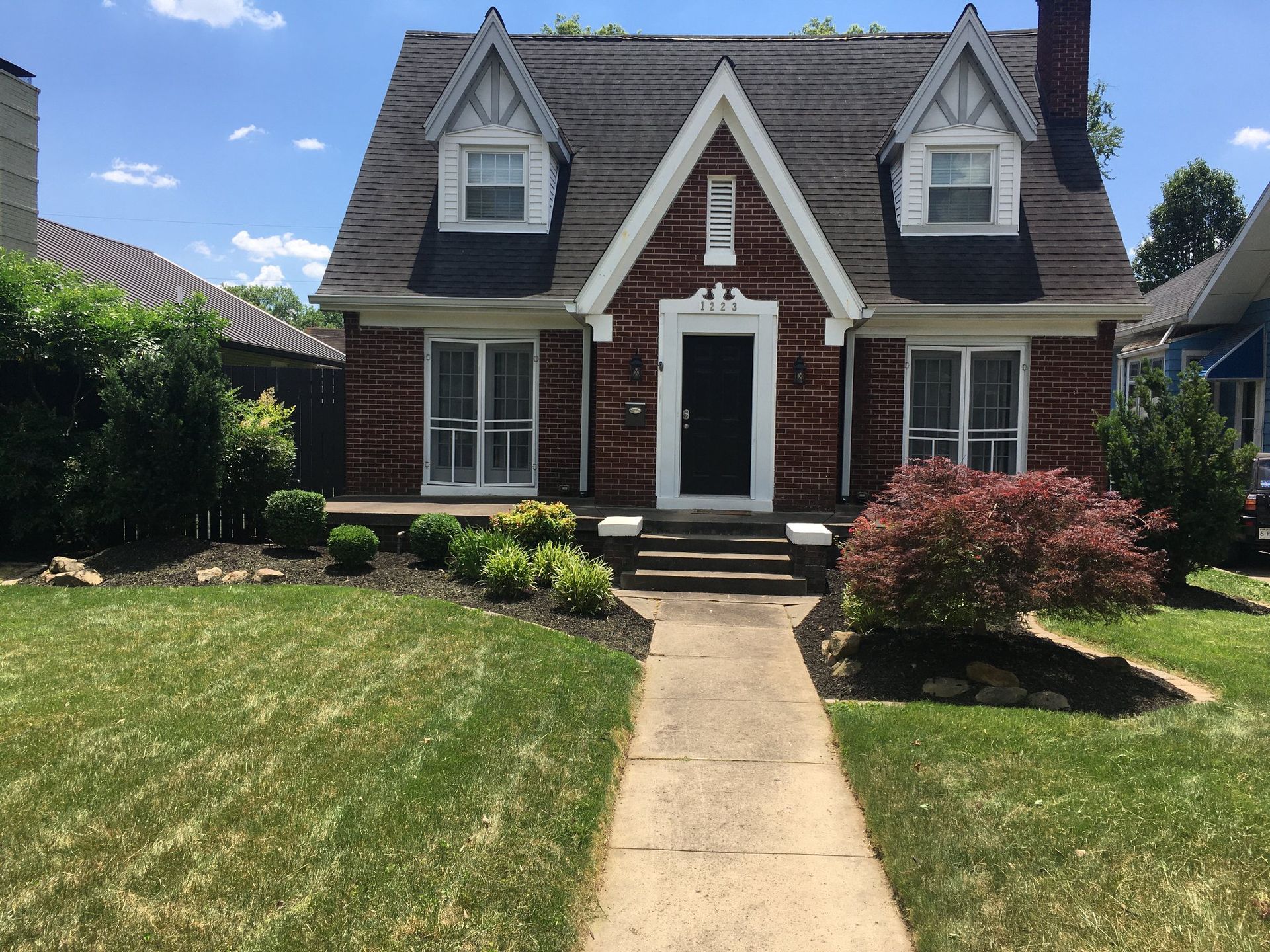 Small brick house with a front lawn, white-trimmed windows, and a central walkway leading to the door