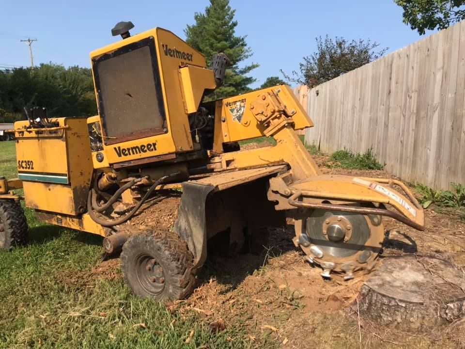 Yellow Vermeer stump grinder with front cutting wheel working on a tree stump in a grassy yard