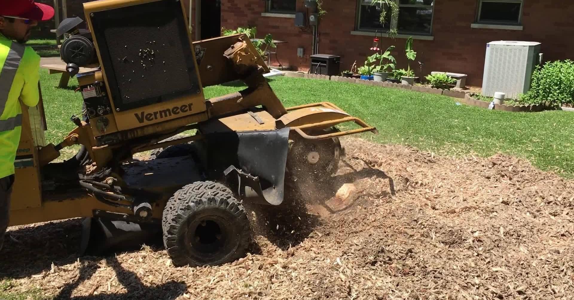 Yellow wood chipper blowing mulch onto a garden bed in a sunny yard