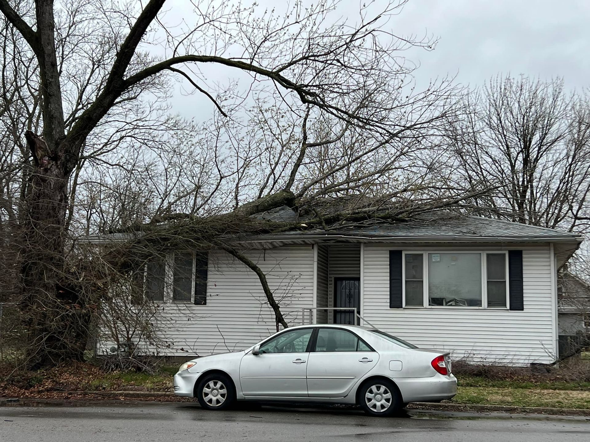 Silver sedan parked in front of a small white house with bare trees around it