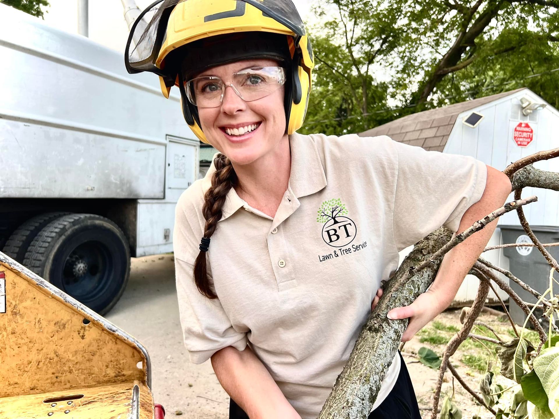 Smiling person in safety gear holding a large fish beside a trailer outdoors