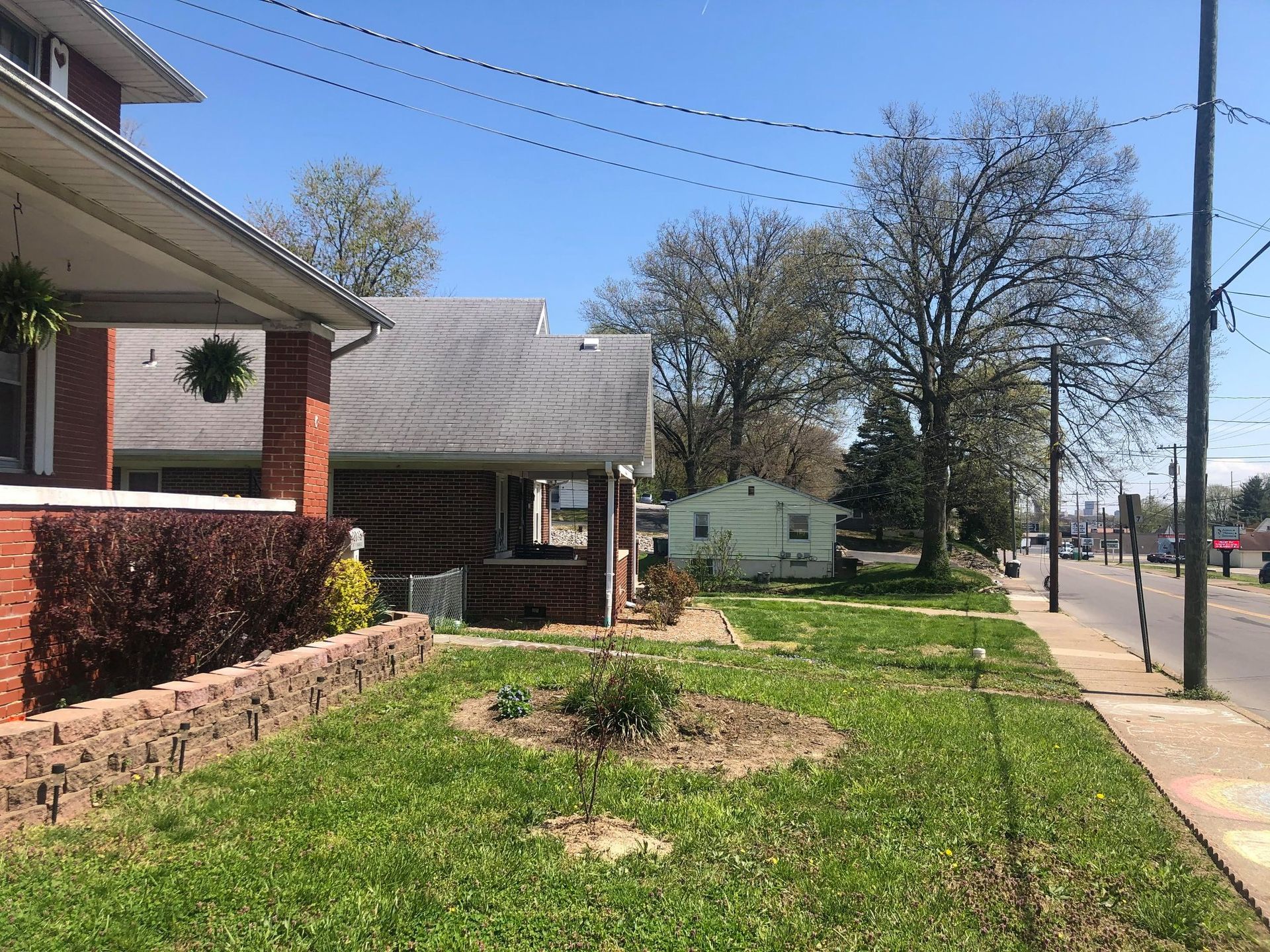 Residential street with houses, a grassy front yard, sidewalk, and utility poles under a clear sky