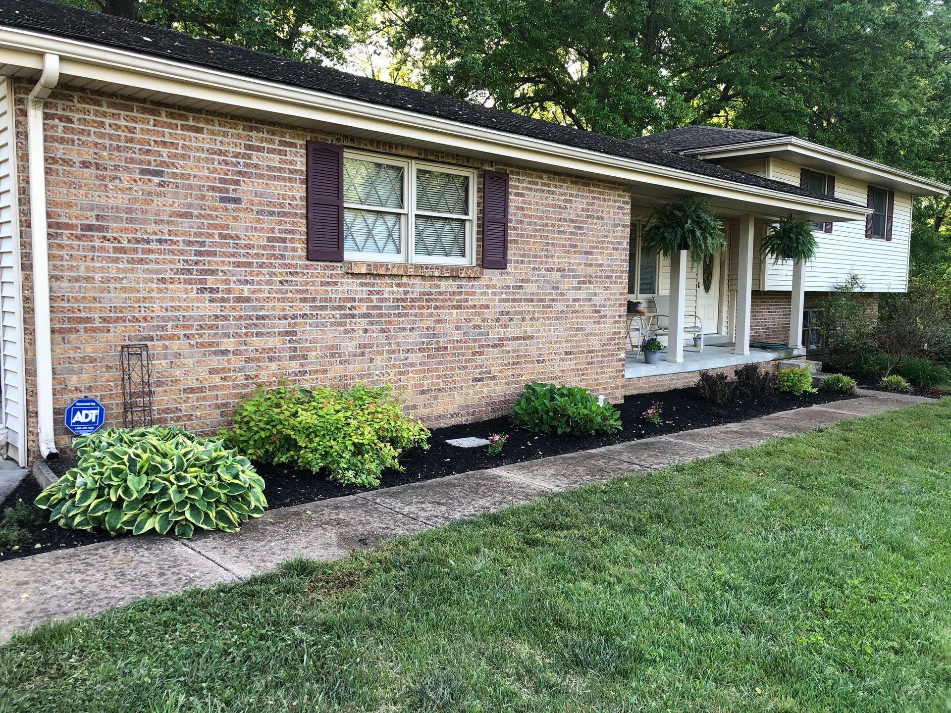 Single-story brick house with white trim, front porch, and landscaped shrubs along the lawn.