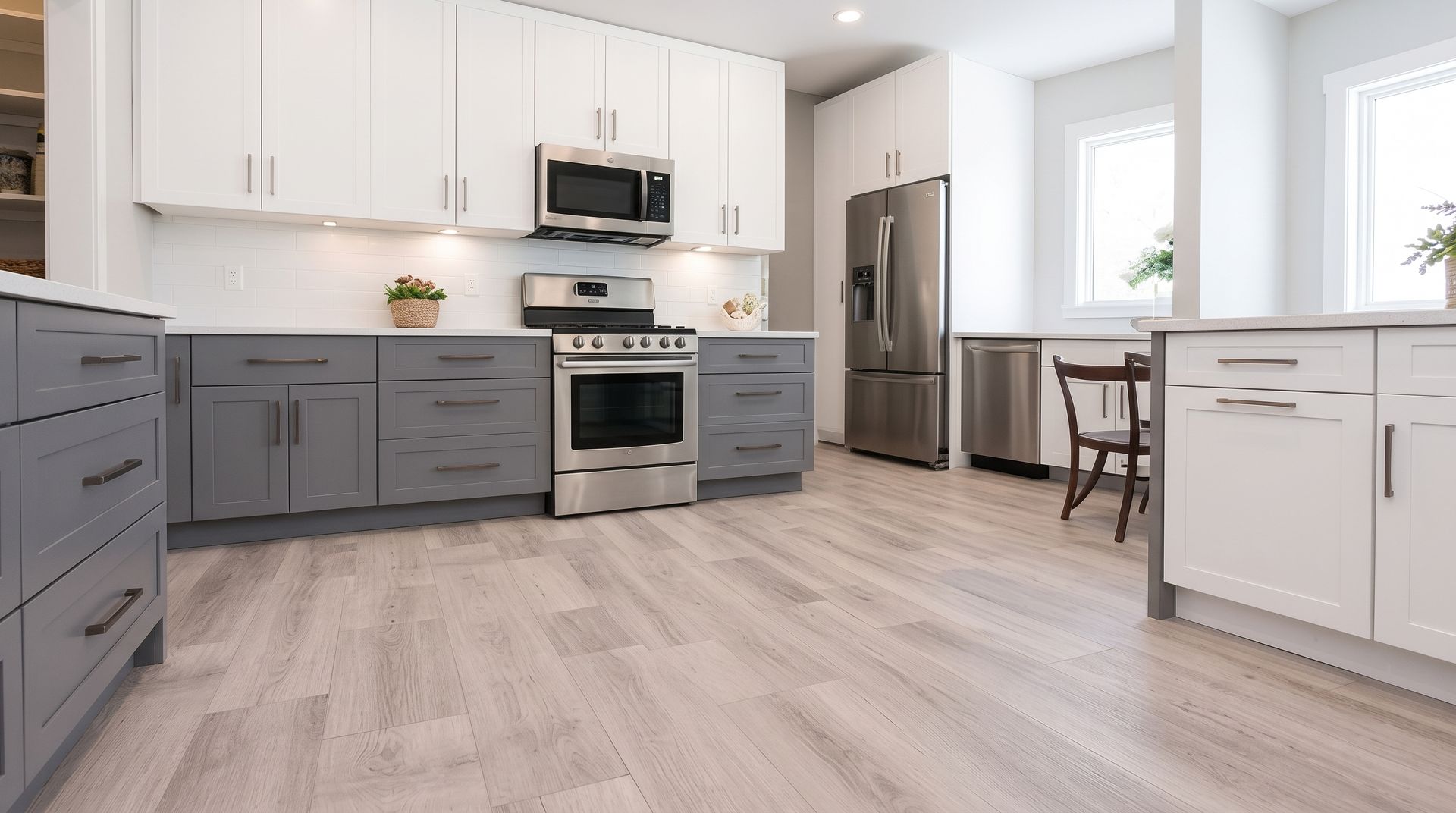 Modern kitchen with white and gray cabinets, stainless appliances, light wood floor, and dining nook by windows