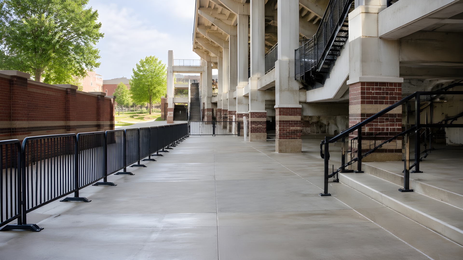 Empty walkway with black railings beside a building and steps, under a shaded colonnade.