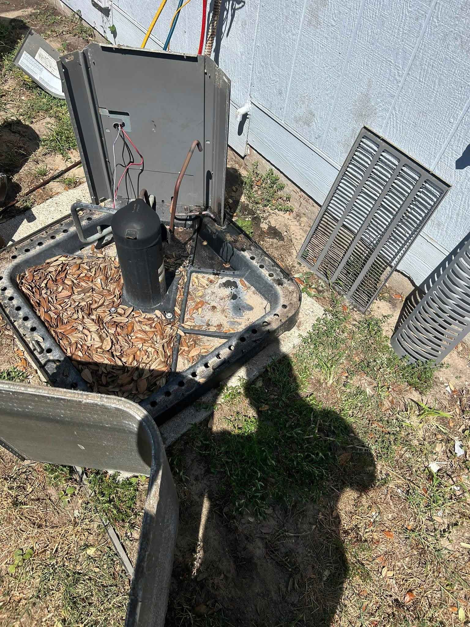 Outdoor air-conditioning unit beside a house, with debris and a damaged metal grate nearby.