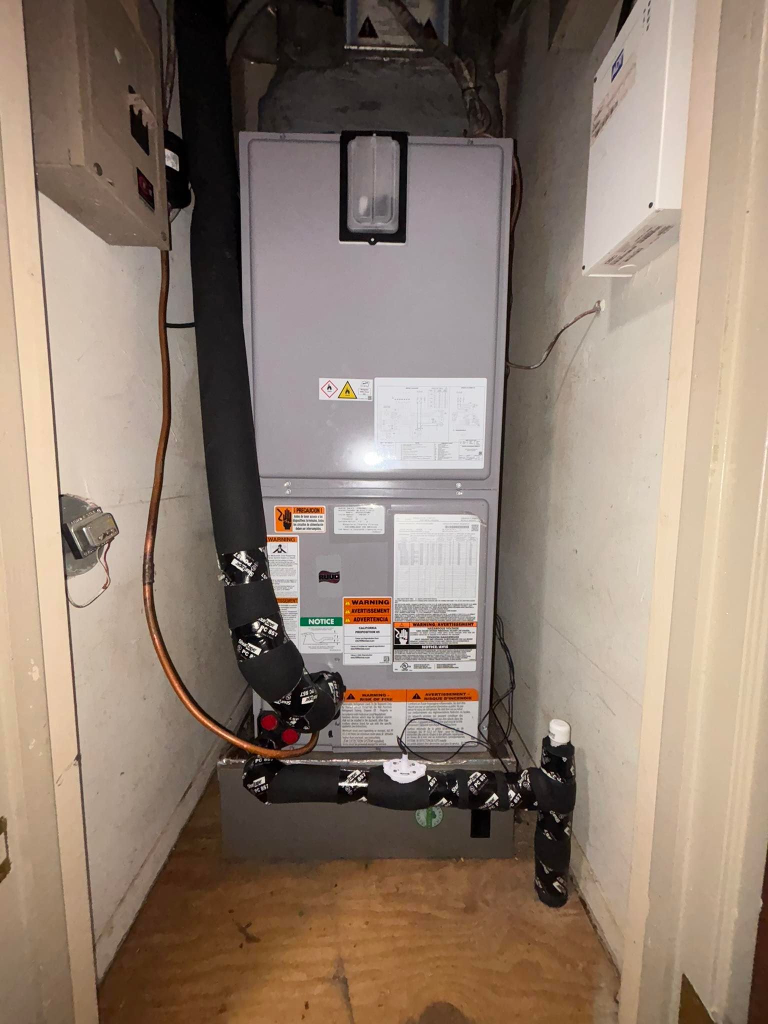 HVAC furnace and connected pipes in a narrow utility closet