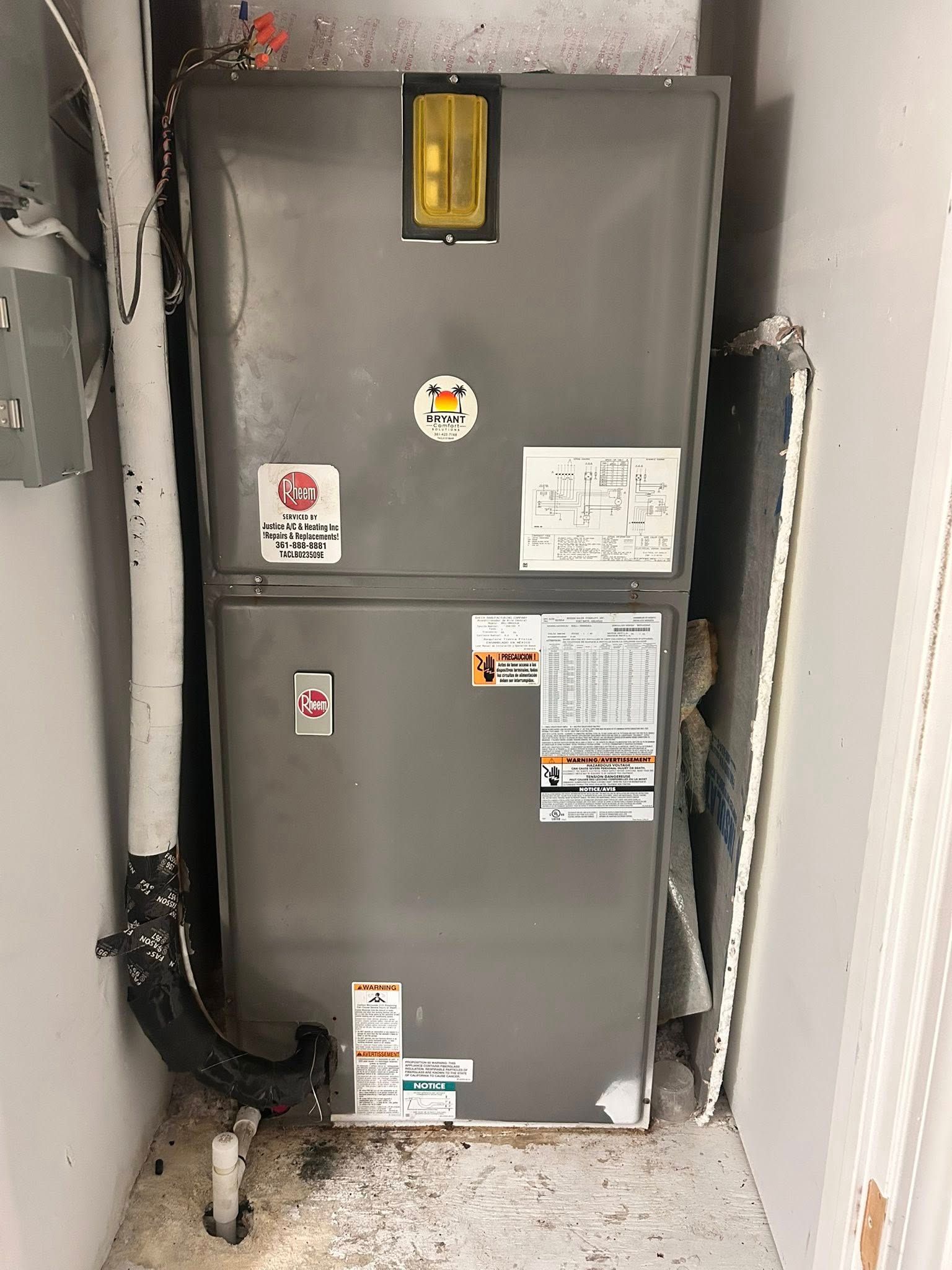 Gray electrical panel in a narrow utility closet with labels and exposed cables.