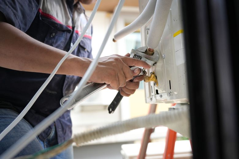 Technician inspecting large silver HVAC ductwork in a bright empty room with a handheld device Technician inspecting large silver HVAC ductwork in a bright empty room with a handheld device