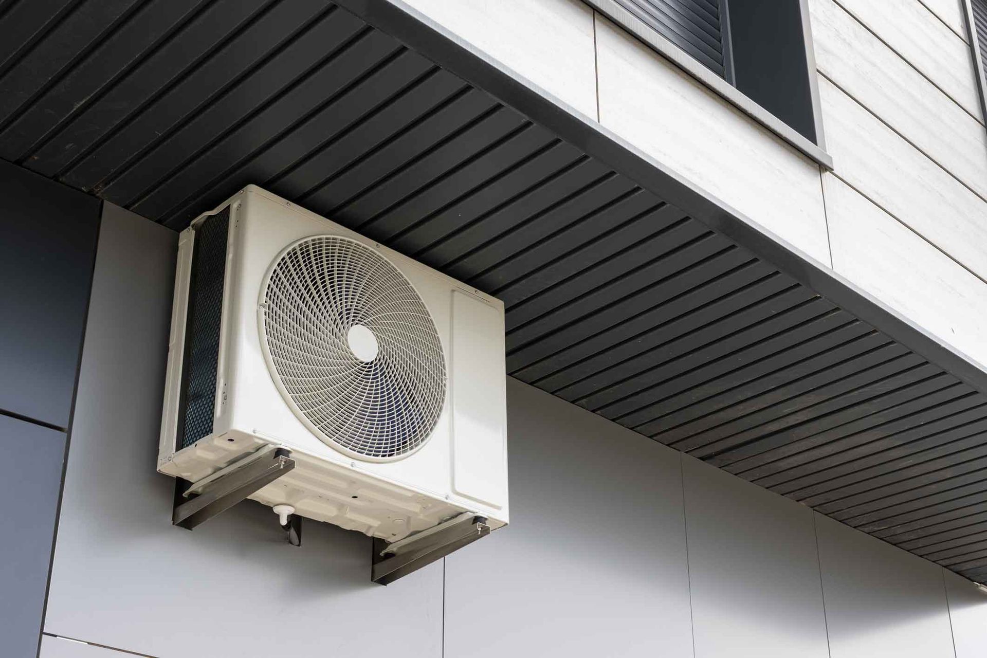 Outdoor air conditioner unit mounted under a building roof overhang