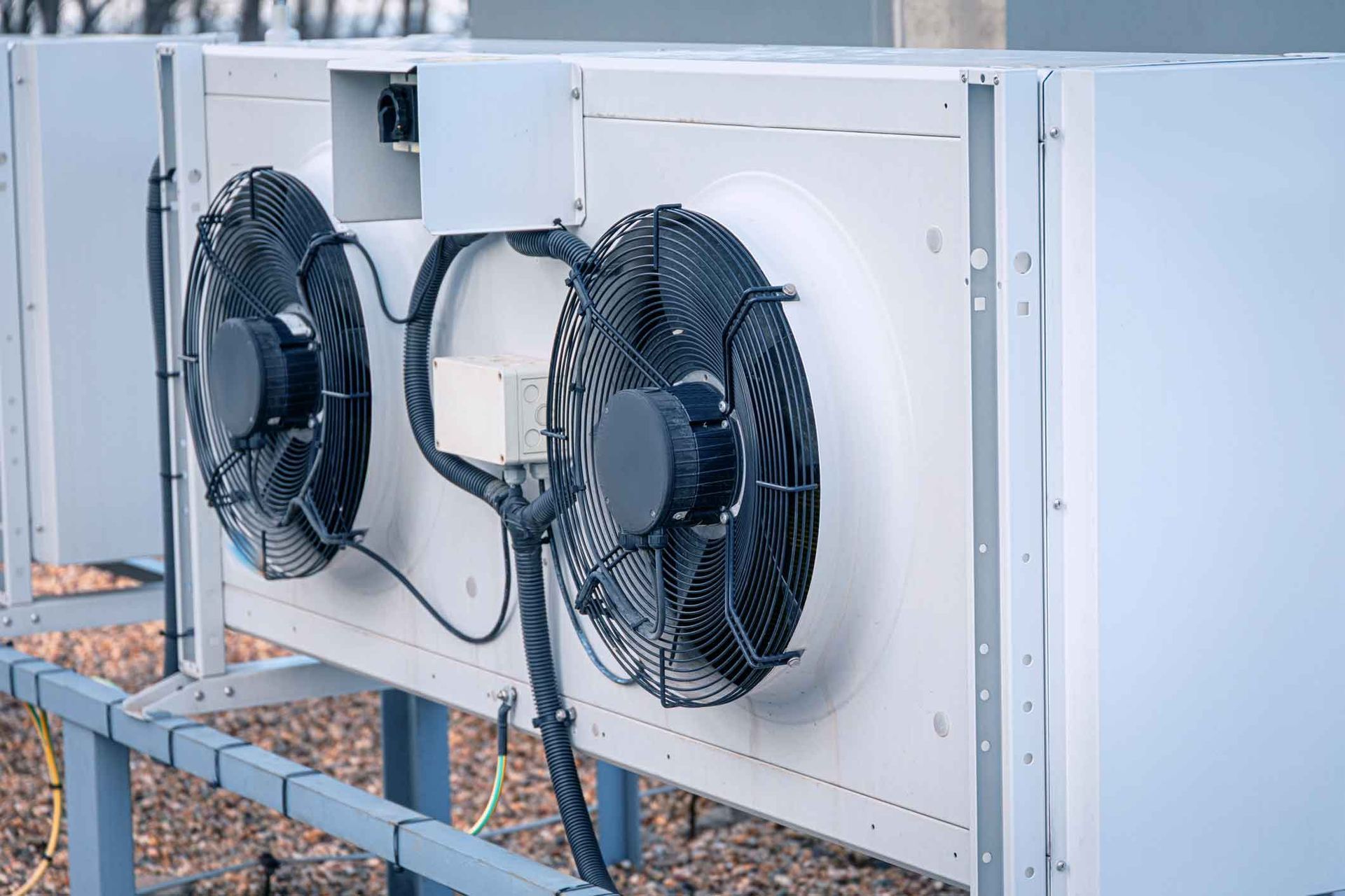 Two black industrial fans mounted on a white outdoor unit on a rooftop platform