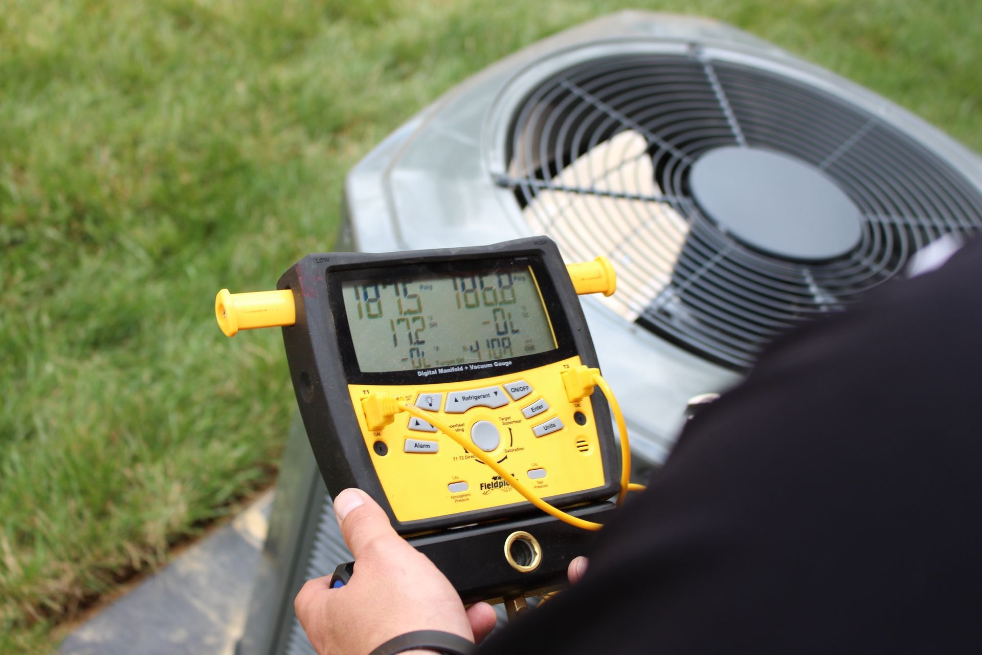 Technician in yellow shirt kneeling to inspect wiring on outdoor HVAC unit Technician in yellow shirt kneeling to inspect wiring on outdoor HVAC unit