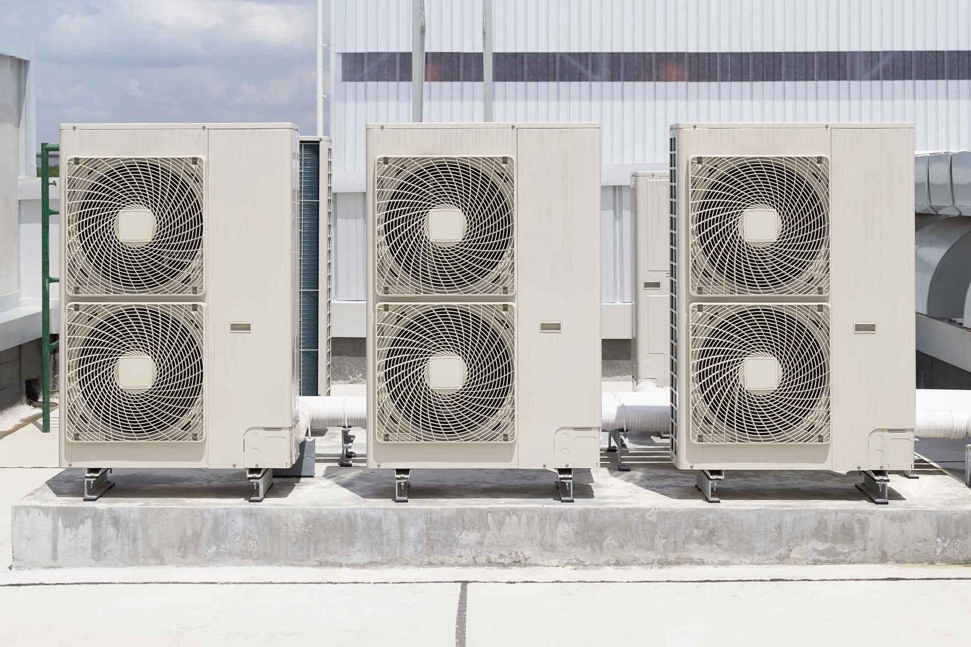 Three outdoor HVAC units with large fans installed on a rooftop or concrete platform.