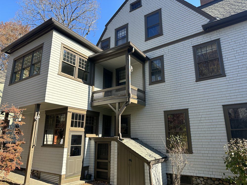 White multi-story house exterior with dark-trim windows and a small central balcony under a clear blue sky