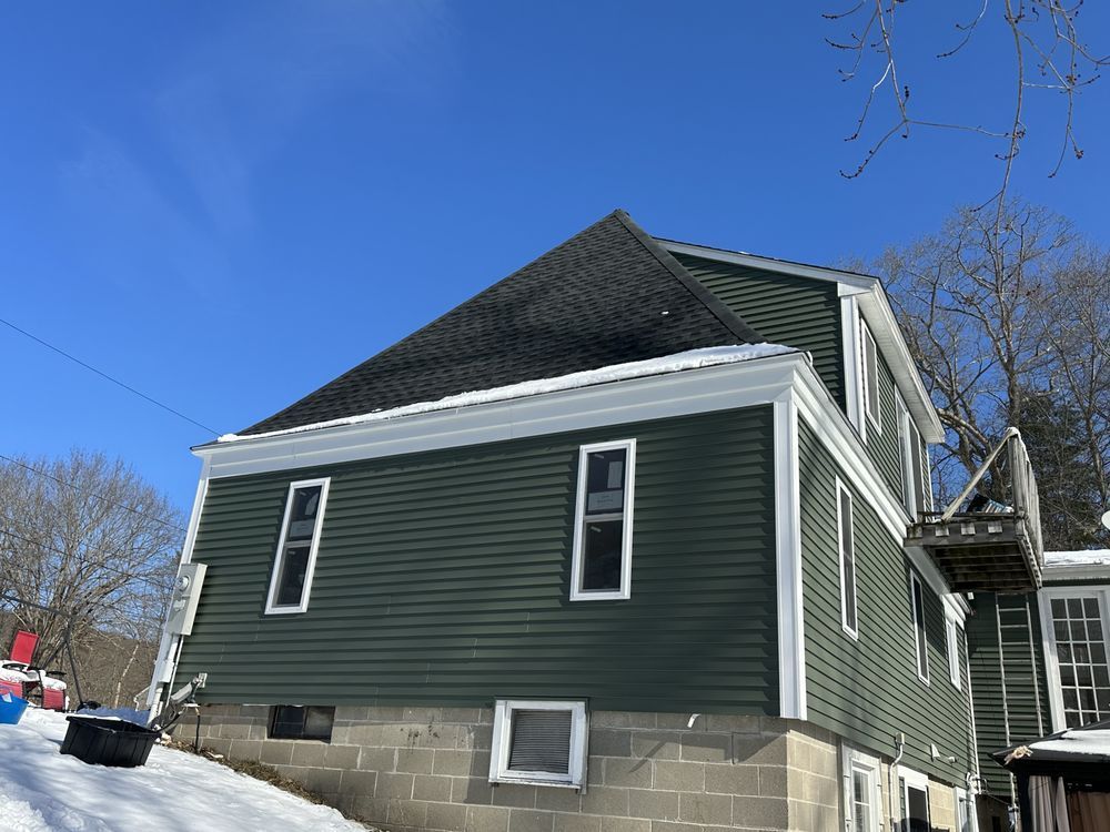 Green house with black roof and white trim on a snowy street under a clear blue sky