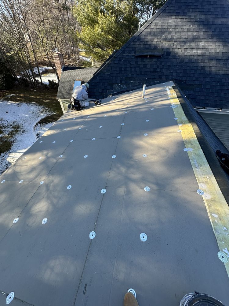 Roof under construction with roofing underlayment and a worker near the edge by the trees