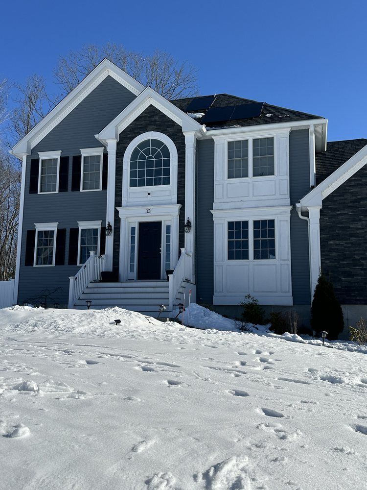 Two-story gray house with white trim and snow-covered yard under a clear blue sky
