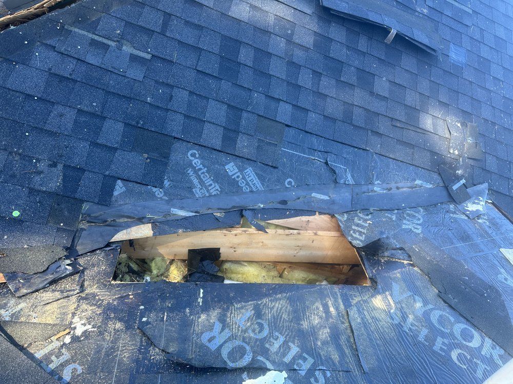 Damaged dark shingle roof with a large hole exposing wooden beams and interior space