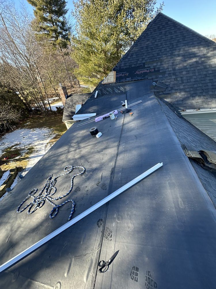 Roof under repair with roofing materials and tools on a house beside trees and snow.