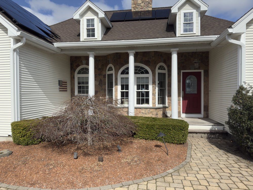 Front porch of a suburban house with white siding, stone columns, arched windows, and a red front door