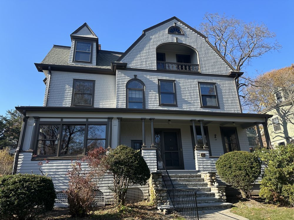 Gray Victorian house with porch, dormer windows, and front steps under a clear blue sky