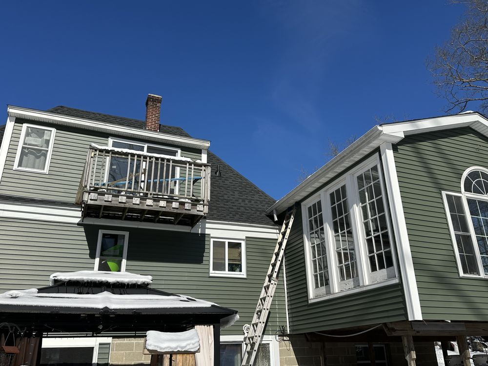 Gray house with a balcony and a ladder leaning to a sunroom under a blue sky