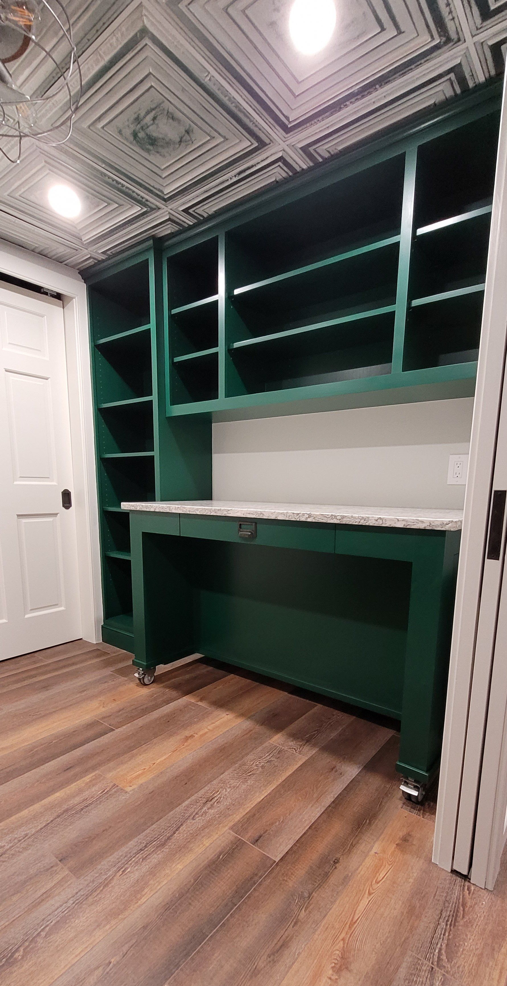 A room with a green desk , shelves , and a ceiling.