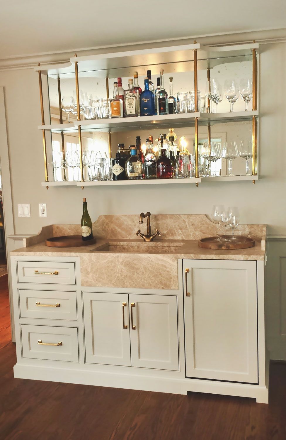 A kitchen with a sink and shelves filled with bottles and glasses.
